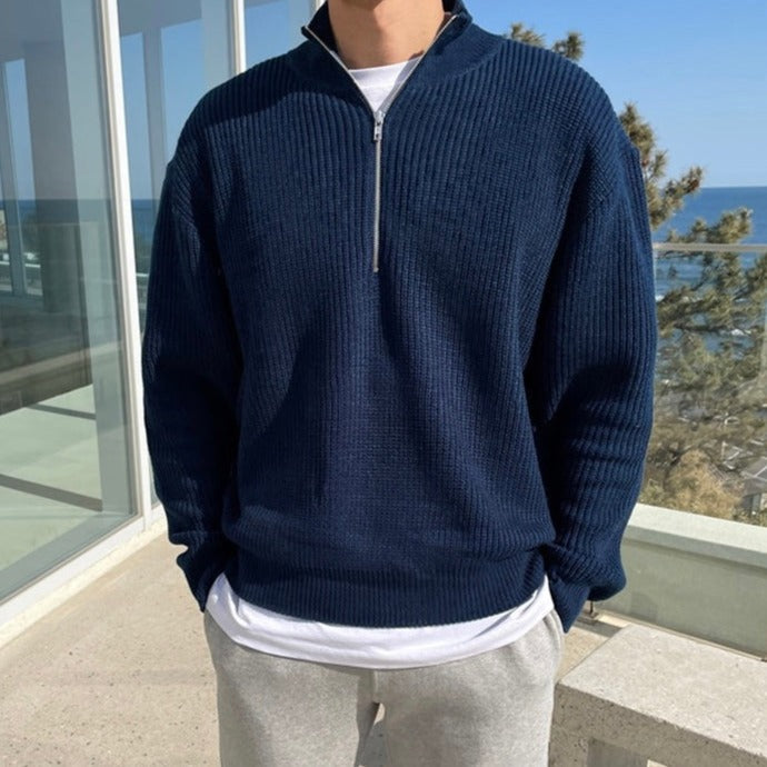 Person wearing a navy blue half-zip sweater with a scenic background