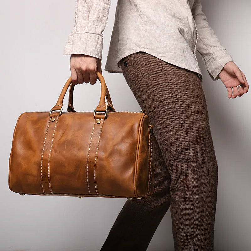 Person holding a brown leather duffel bag against a plain background
