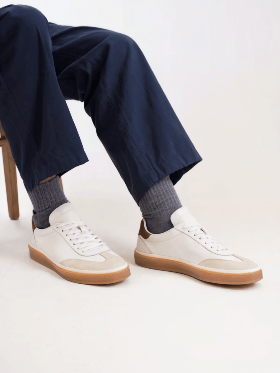 Person wearing navy pants and white sneakers with brown soles on a light background