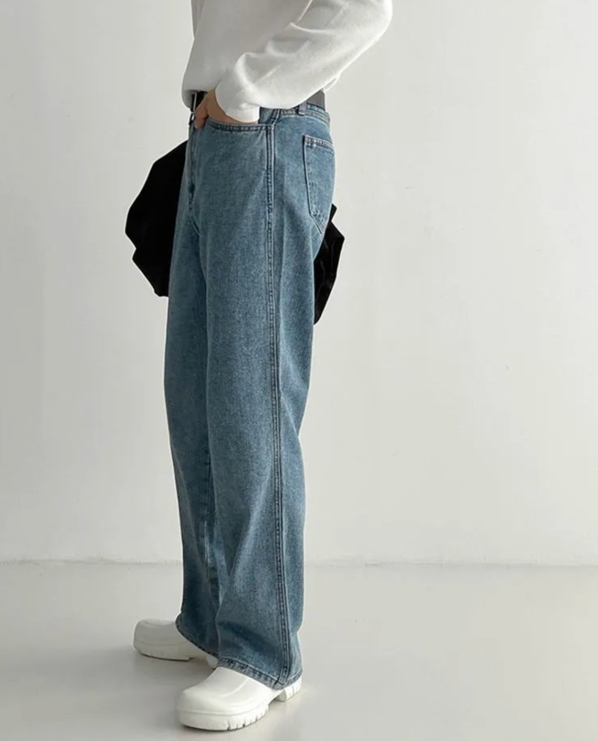 Person wearing blue jeans and a white sweater on a plain background