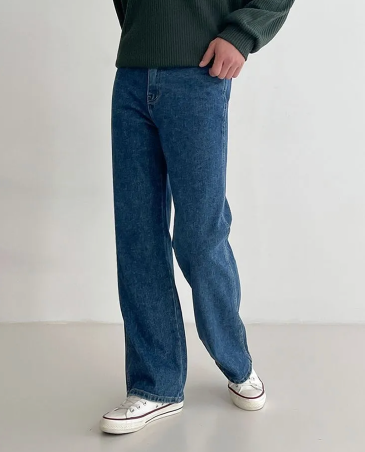 Person wearing blue jeans and a green sweater on a plain background