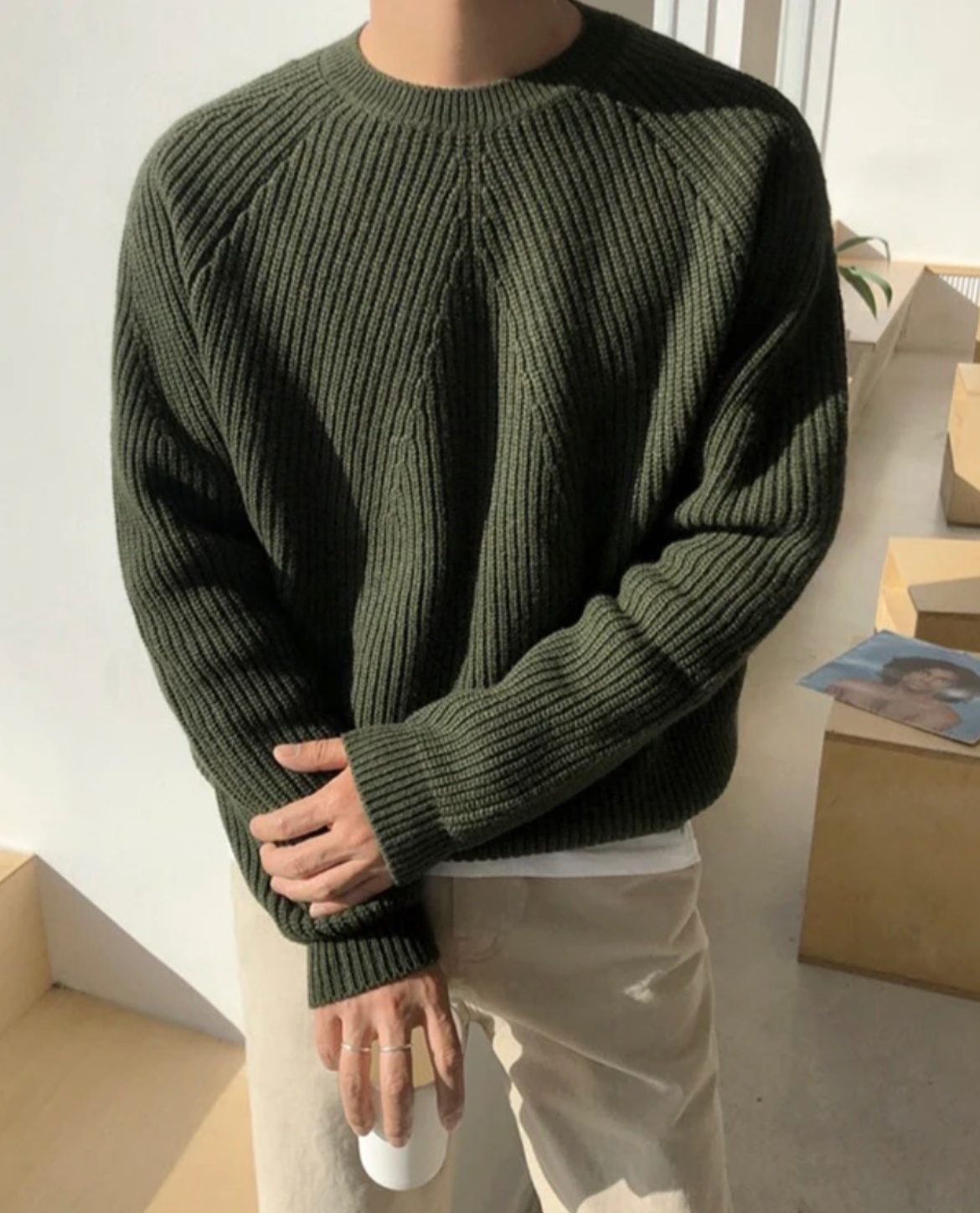 Person wearing a green sweater with a black collar in an indoor setting