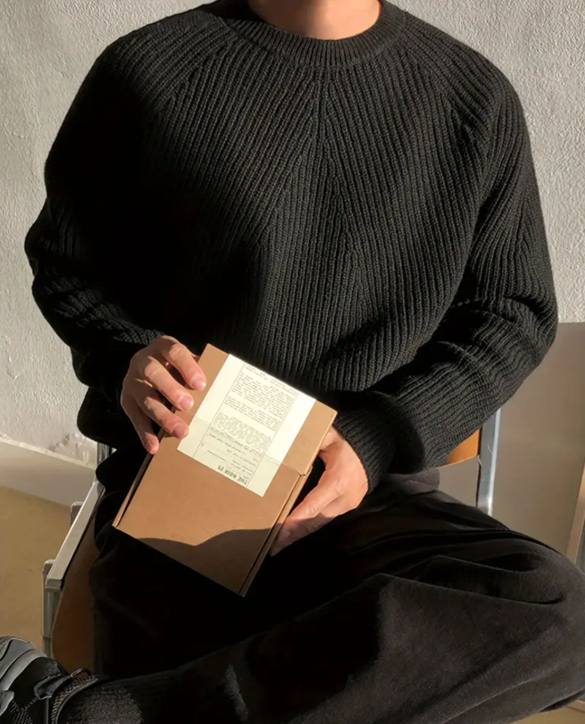 Person wearing a black sweater holding a brown envelope with a white paper inside.