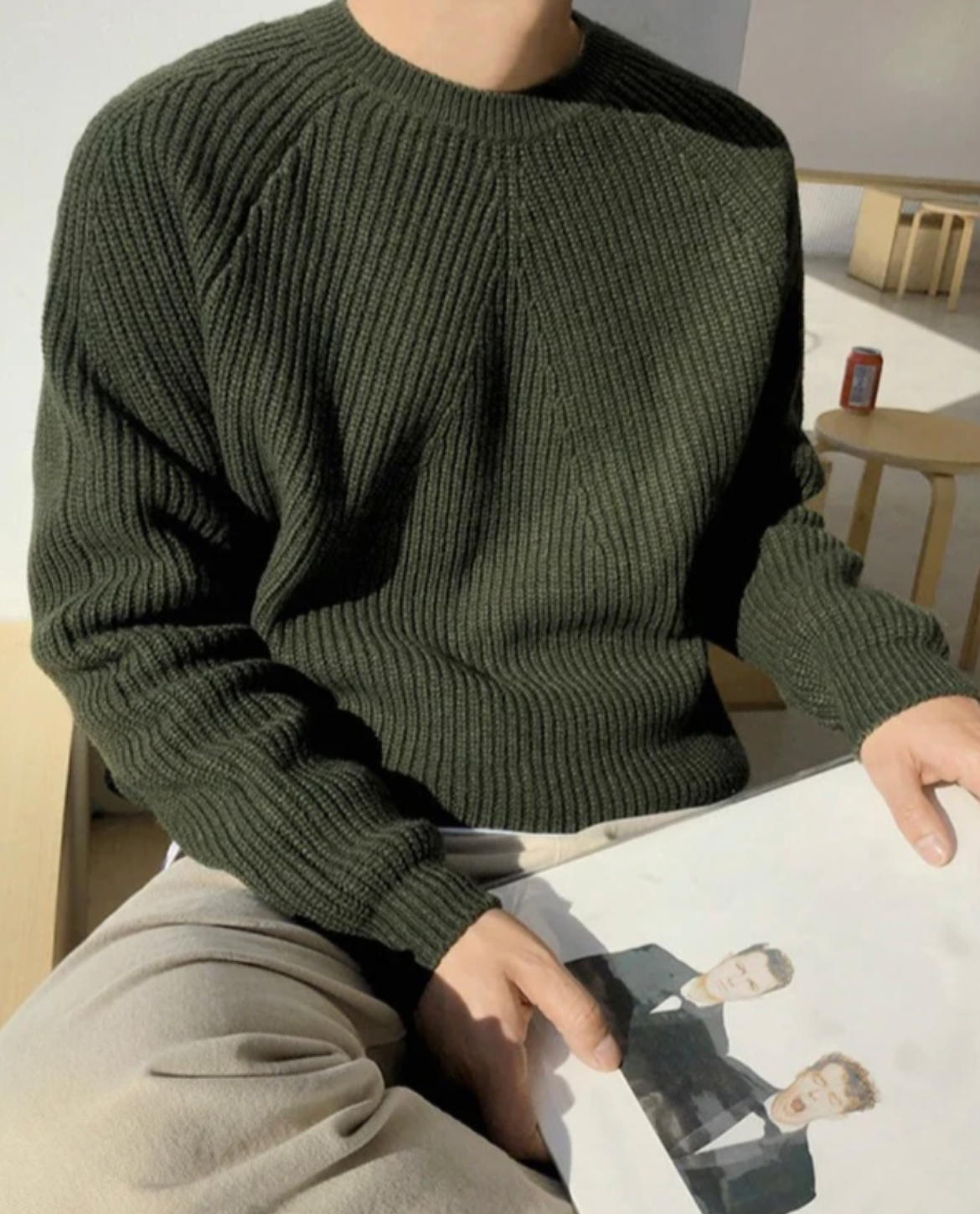 Person wearing a green sweater holding a magazine with a blurred background