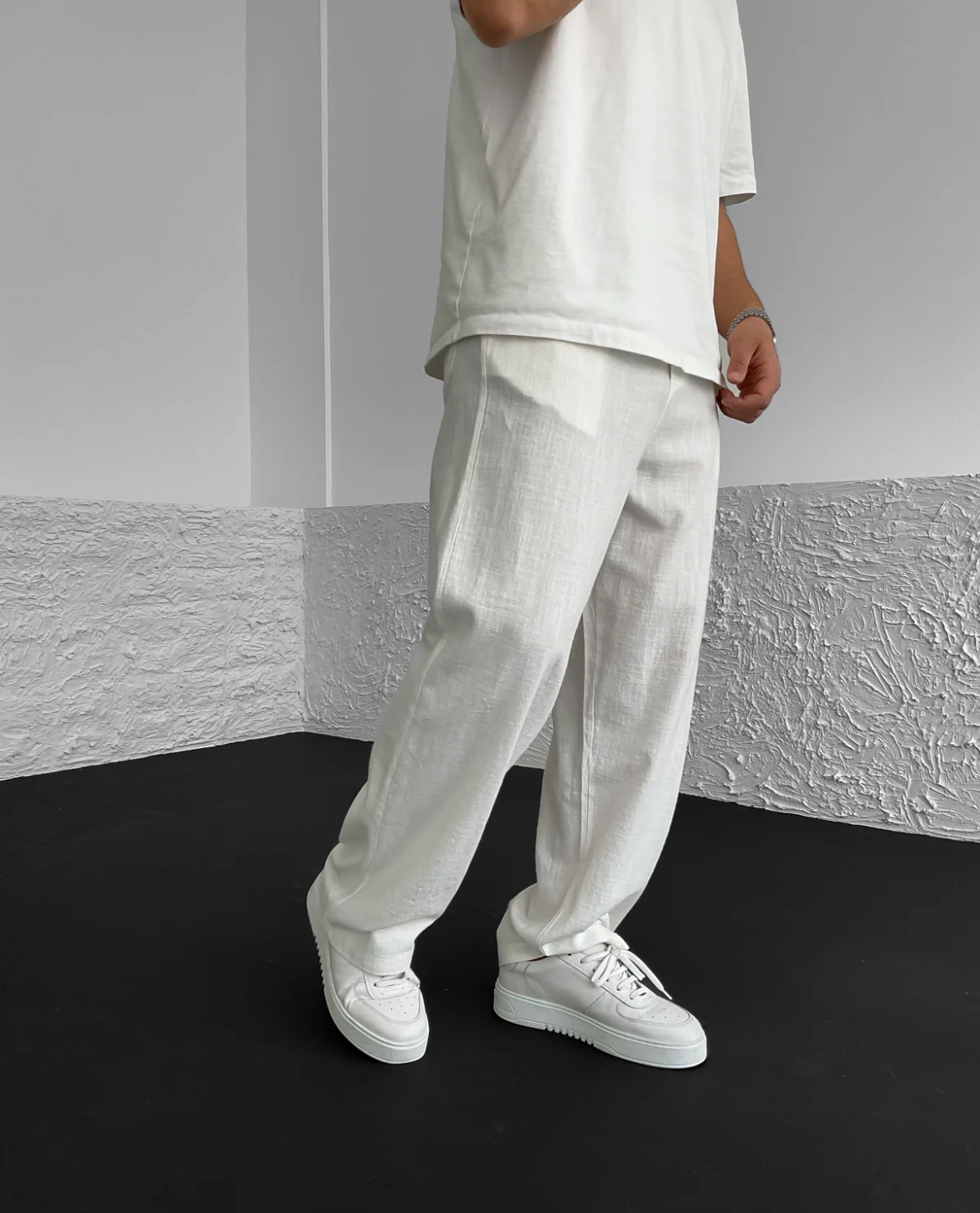Person wearing a white outfit with wide-leg pants against a gray wall.
