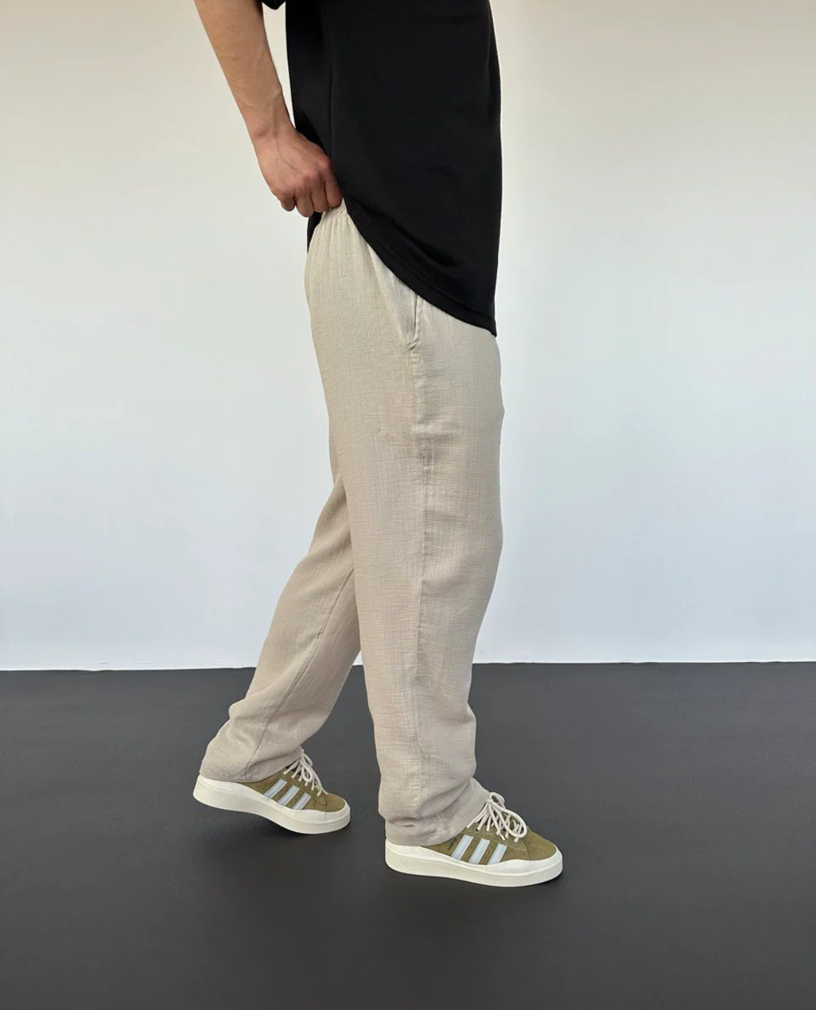 Person wearing beige pants and black shirt with Adidas shoes on a plain background