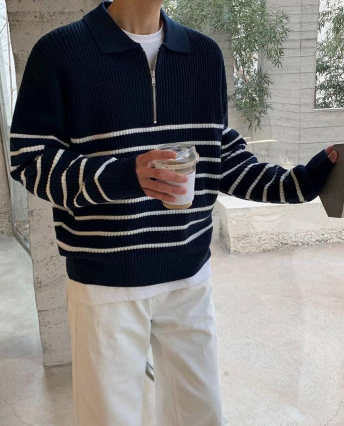 Person wearing a navy and white striped sweater holding a glass outdoors.