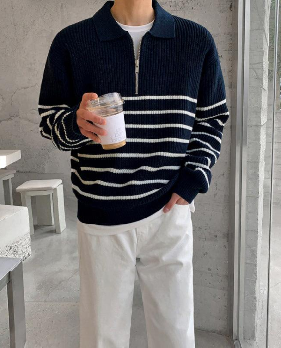 Person wearing a navy and white striped sweater holding a container in a minimalistic room.
