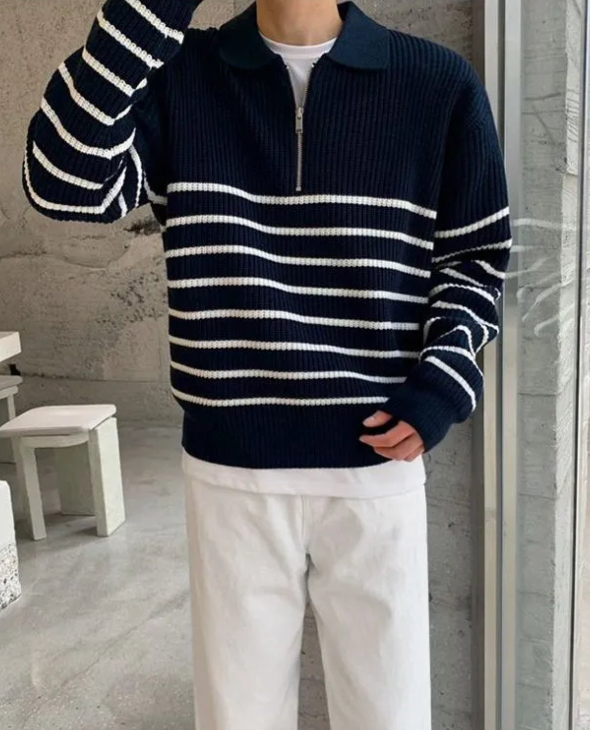 Person wearing a navy and white striped sweater with a zipper, standing indoors.