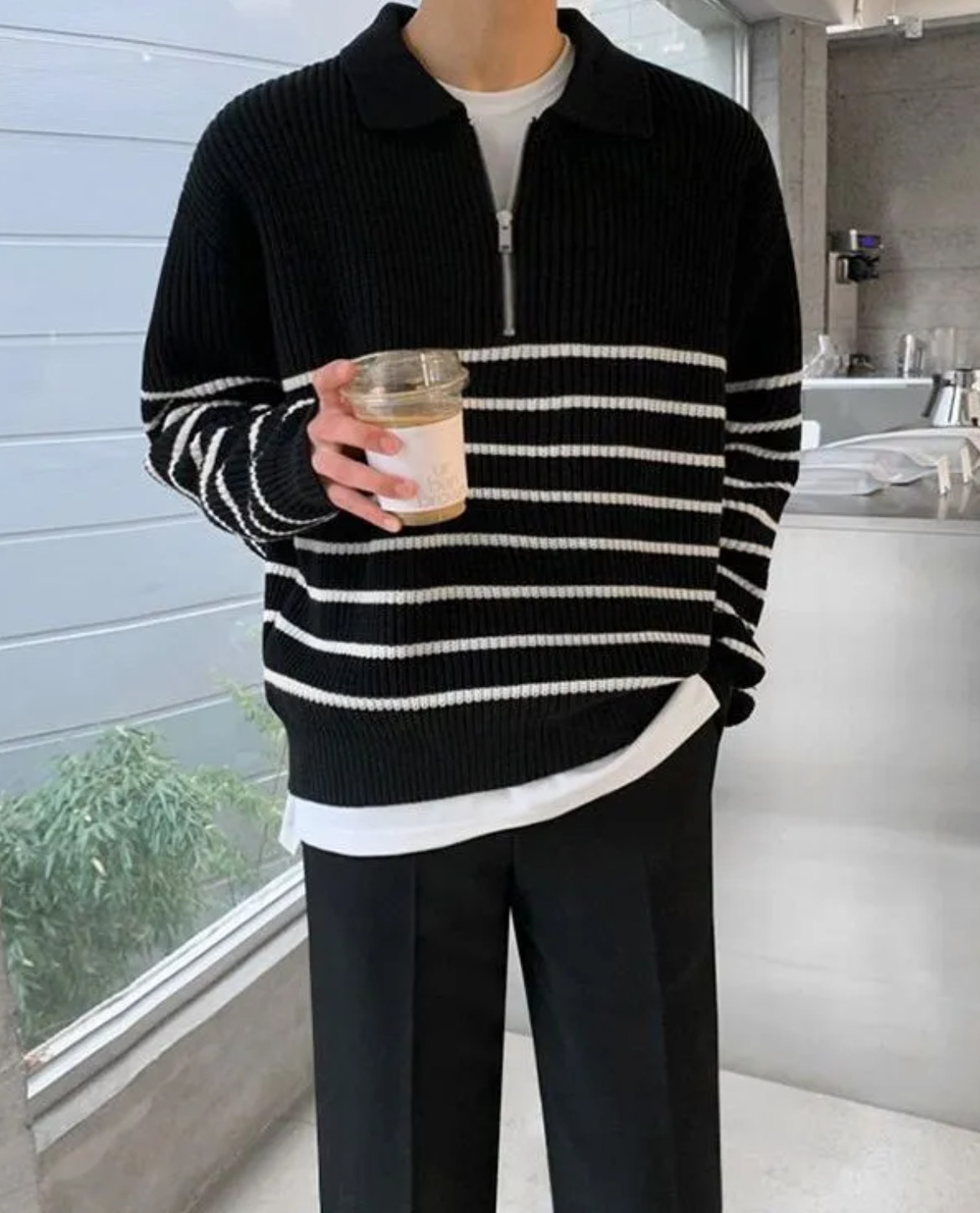 Person wearing a black and white striped sweater holding a cup indoors.