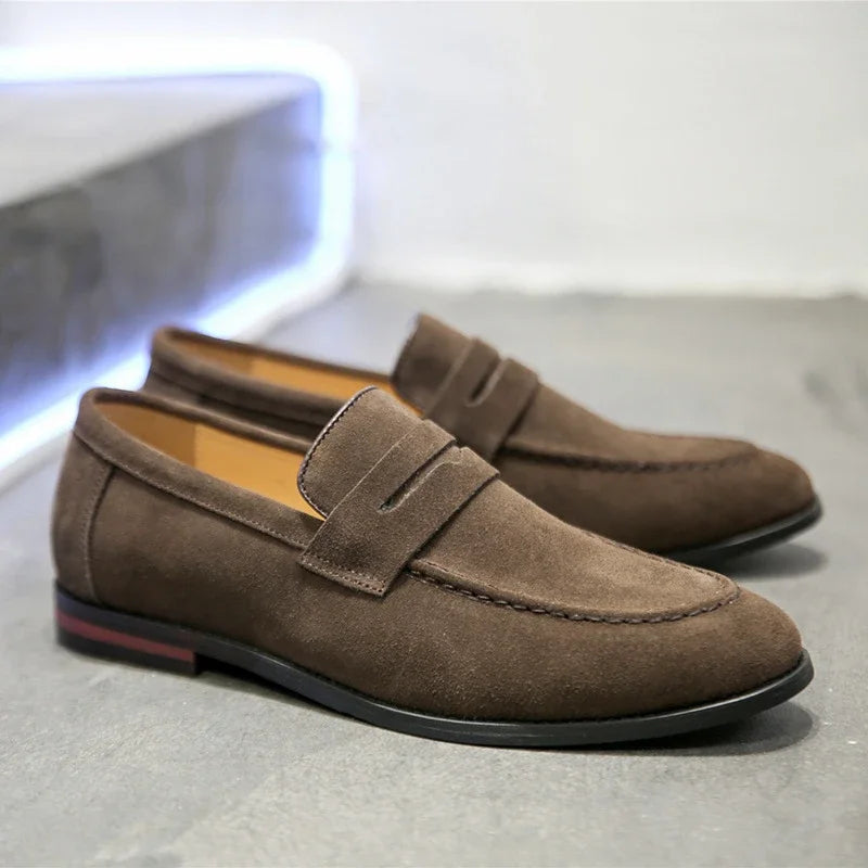 Pair of brown suede loafers on a reflective surface with a blurred background