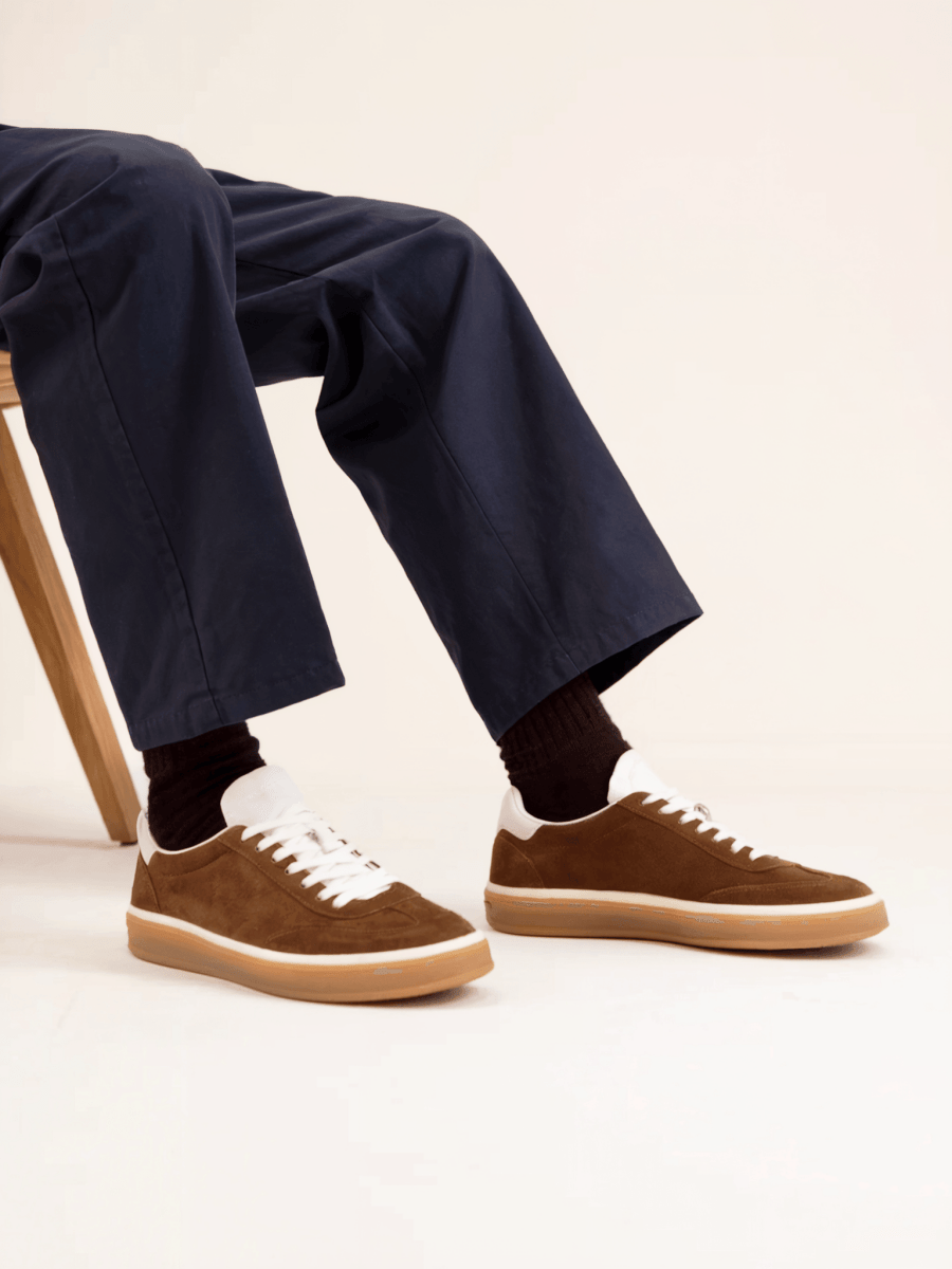 Brown sneakers with white laces worn with navy pants on a light background