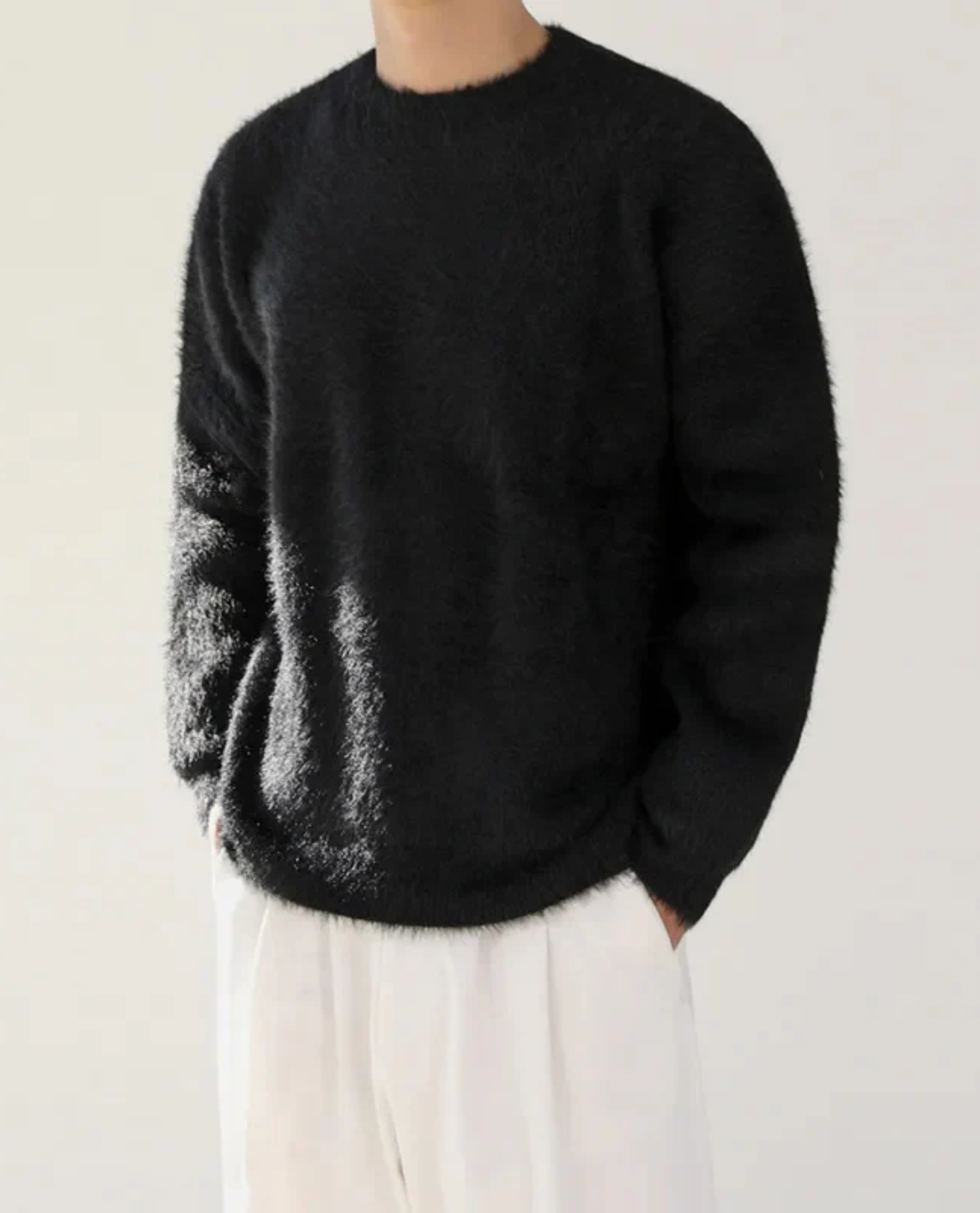 Person wearing a black sweater and white pants against a plain background