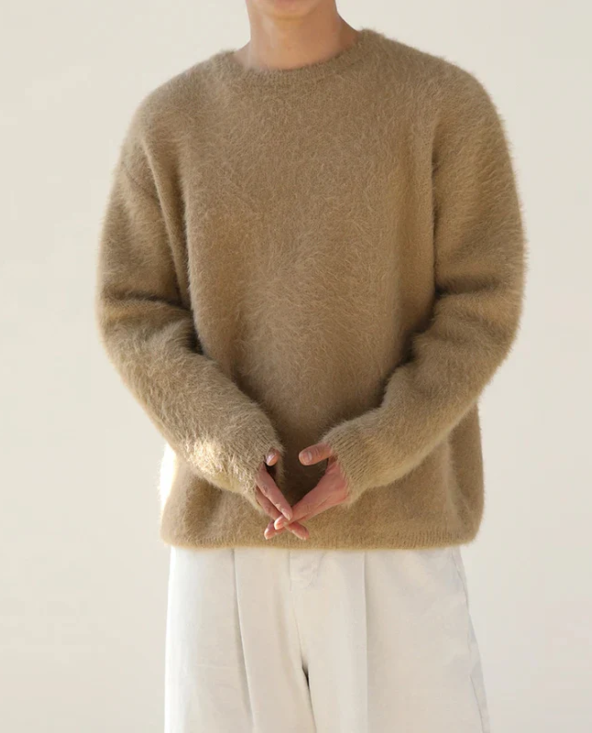 Person wearing a beige sweater with a plain background