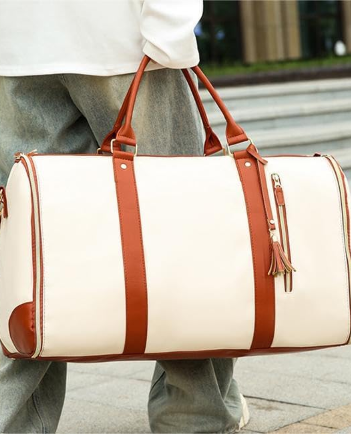 Person holding a white duffel bag with brown straps outdoors.