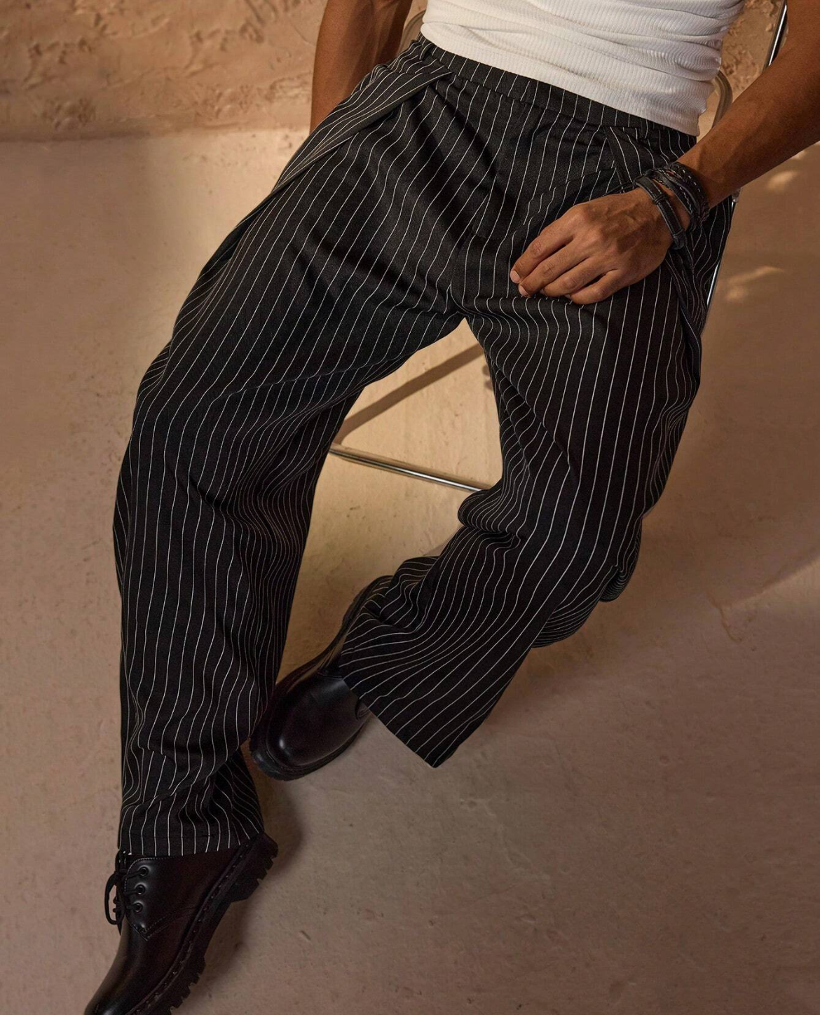 Person wearing black pinstripe pants and shiny shoes on a beige floor.