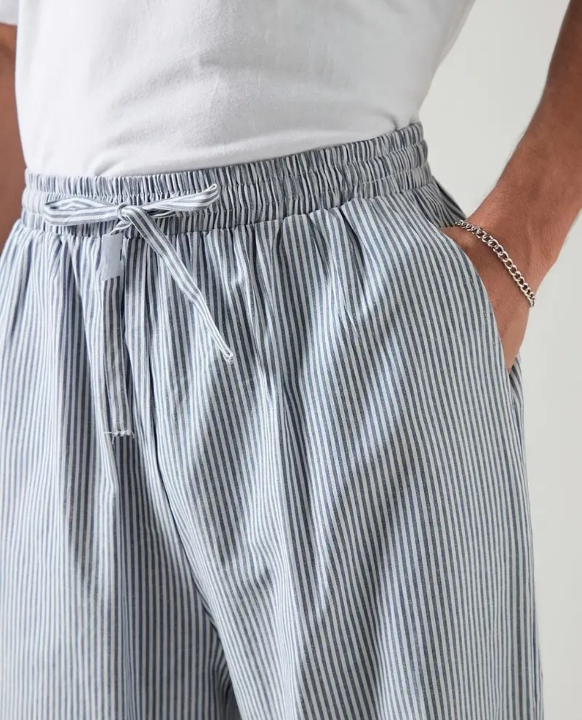 Person wearing gray and white striped pants with a drawstring on a plain background