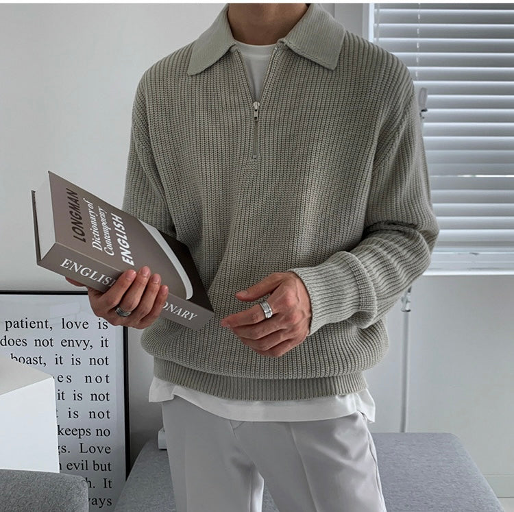 Person wearing a gray sweater holding an open book indoors.