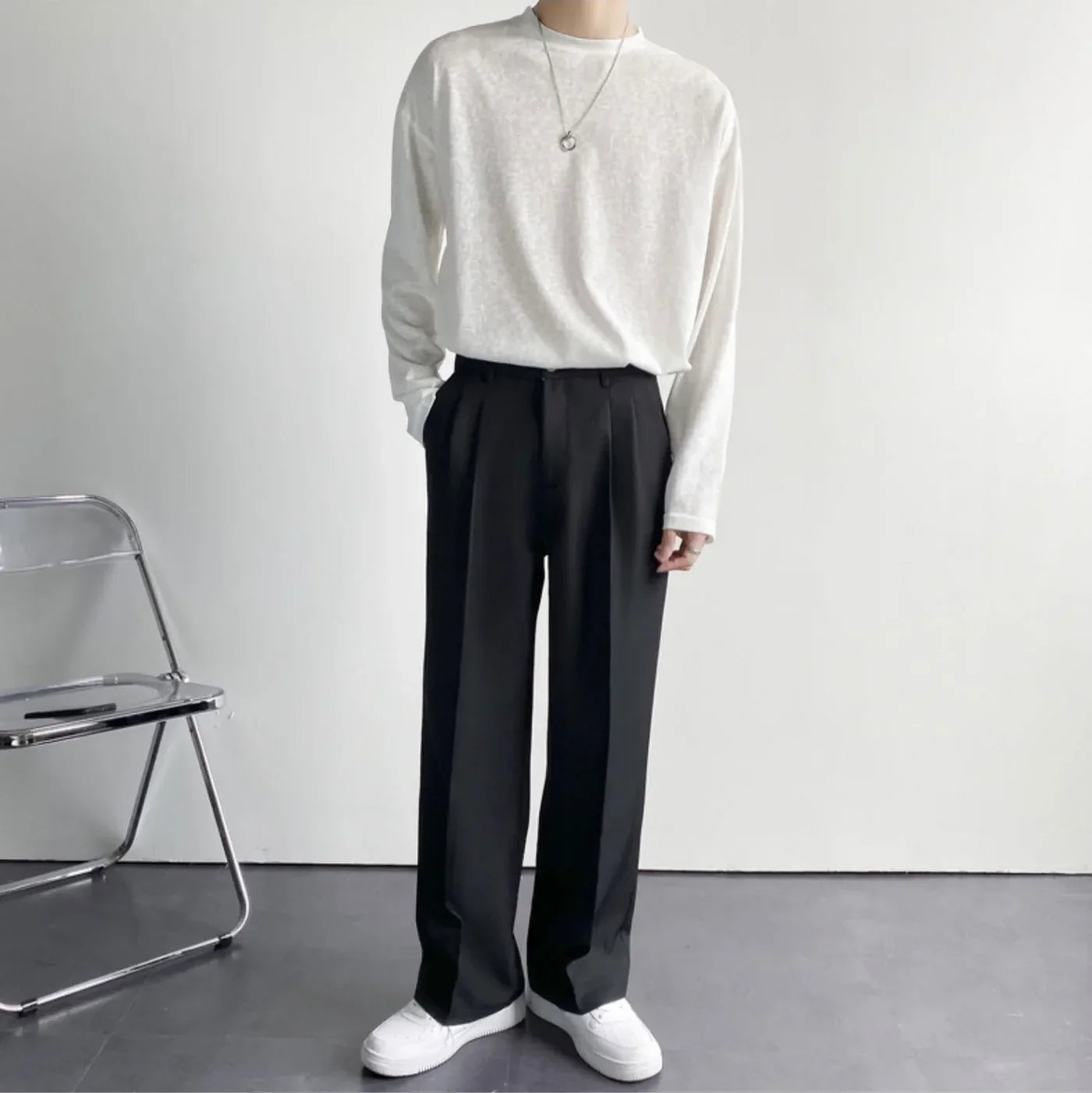 Person wearing a white long-sleeve shirt and black pants standing against a plain background.