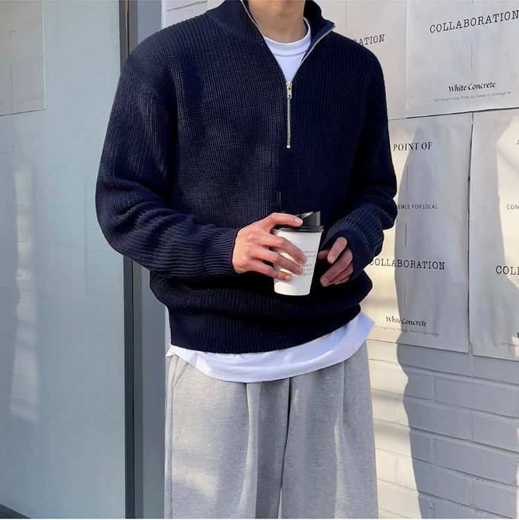 Person wearing a navy blue sweater with a zipper, holding a coffee cup, standing in front of a store entrance.