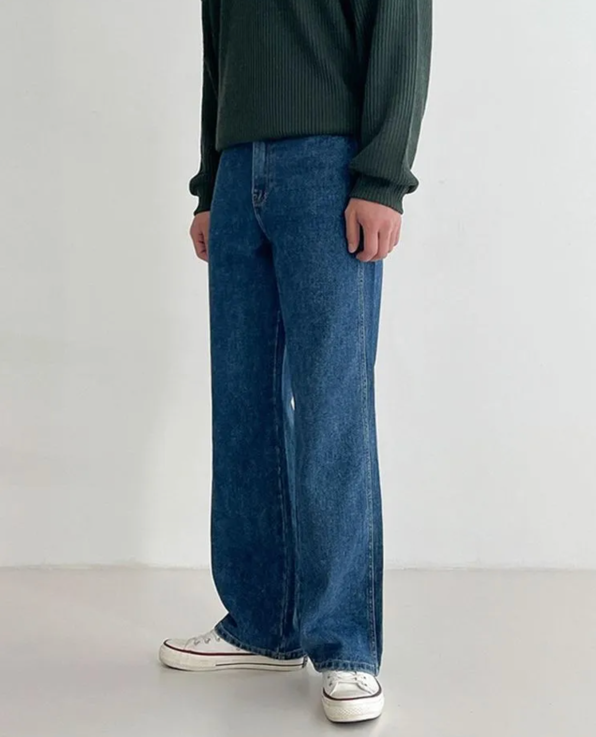Person wearing blue jeans and a dark green sweater on a white background