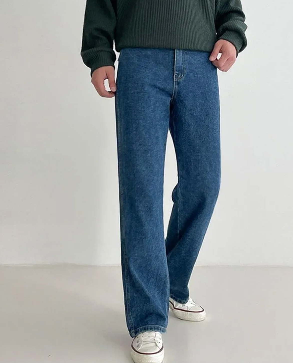 Person wearing blue jeans and a green sweater on a white background
