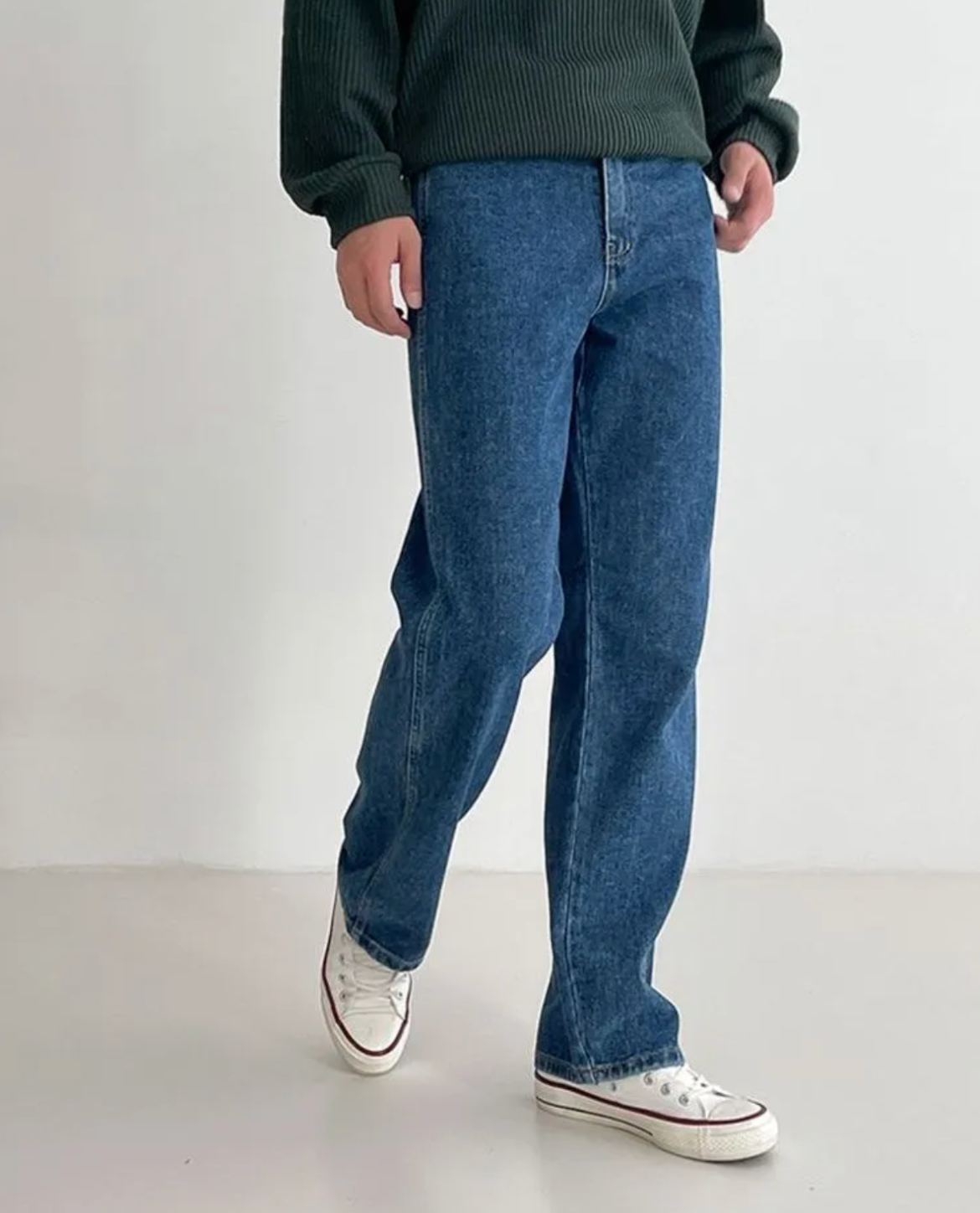 Person wearing blue jeans and a green sweater on a white background