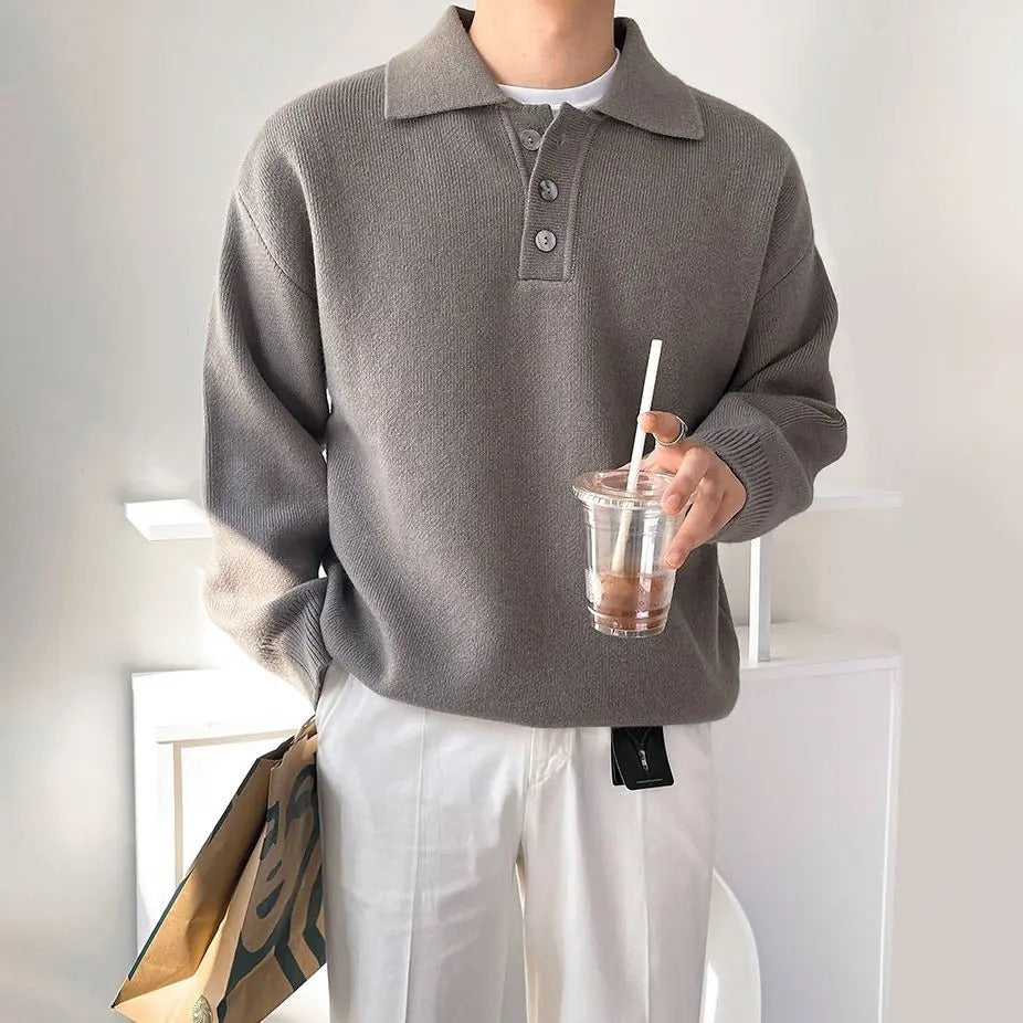 Person wearing a gray sweater holding a drink with a straw indoors.