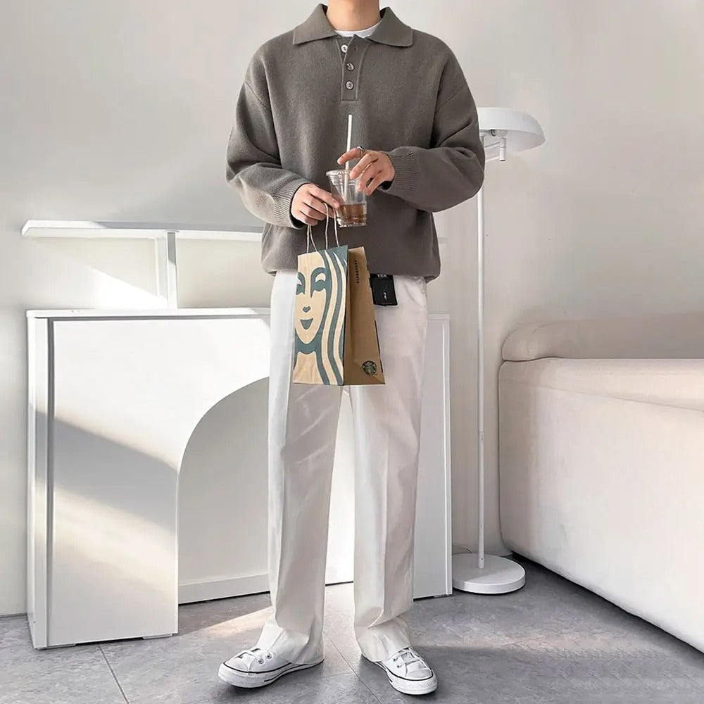 Person wearing a brown sweater and white pants holding a drink and a bag in a modern interior setting.