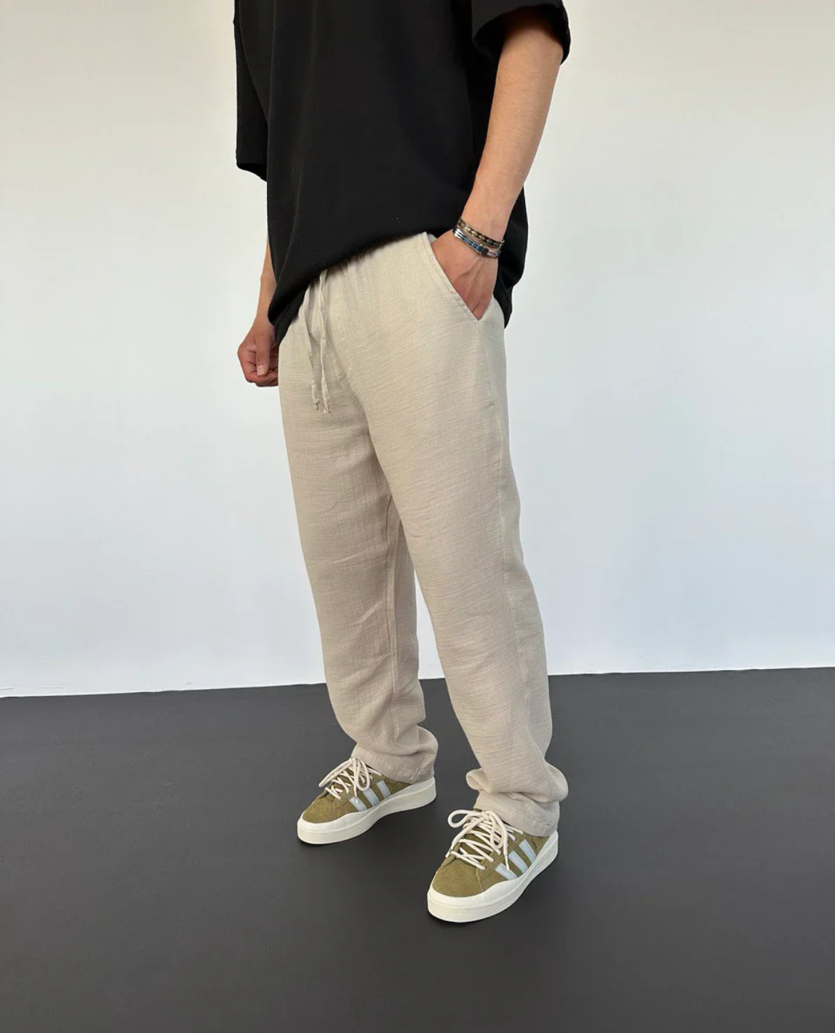 Person wearing beige sweatpants and green sneakers on a plain background
