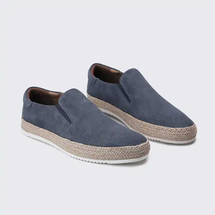 Pair of blue slip-on shoes with jute sole on a light gray background