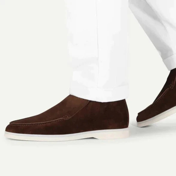 Brown loafers worn with white pants on a light gray background