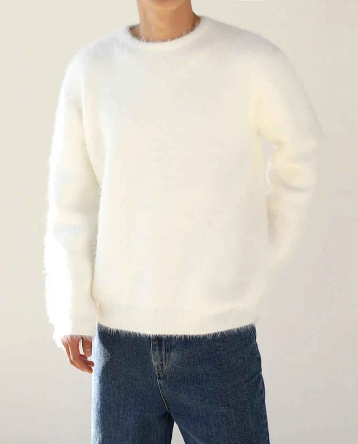 Person wearing a white sweater and blue jeans against a plain background