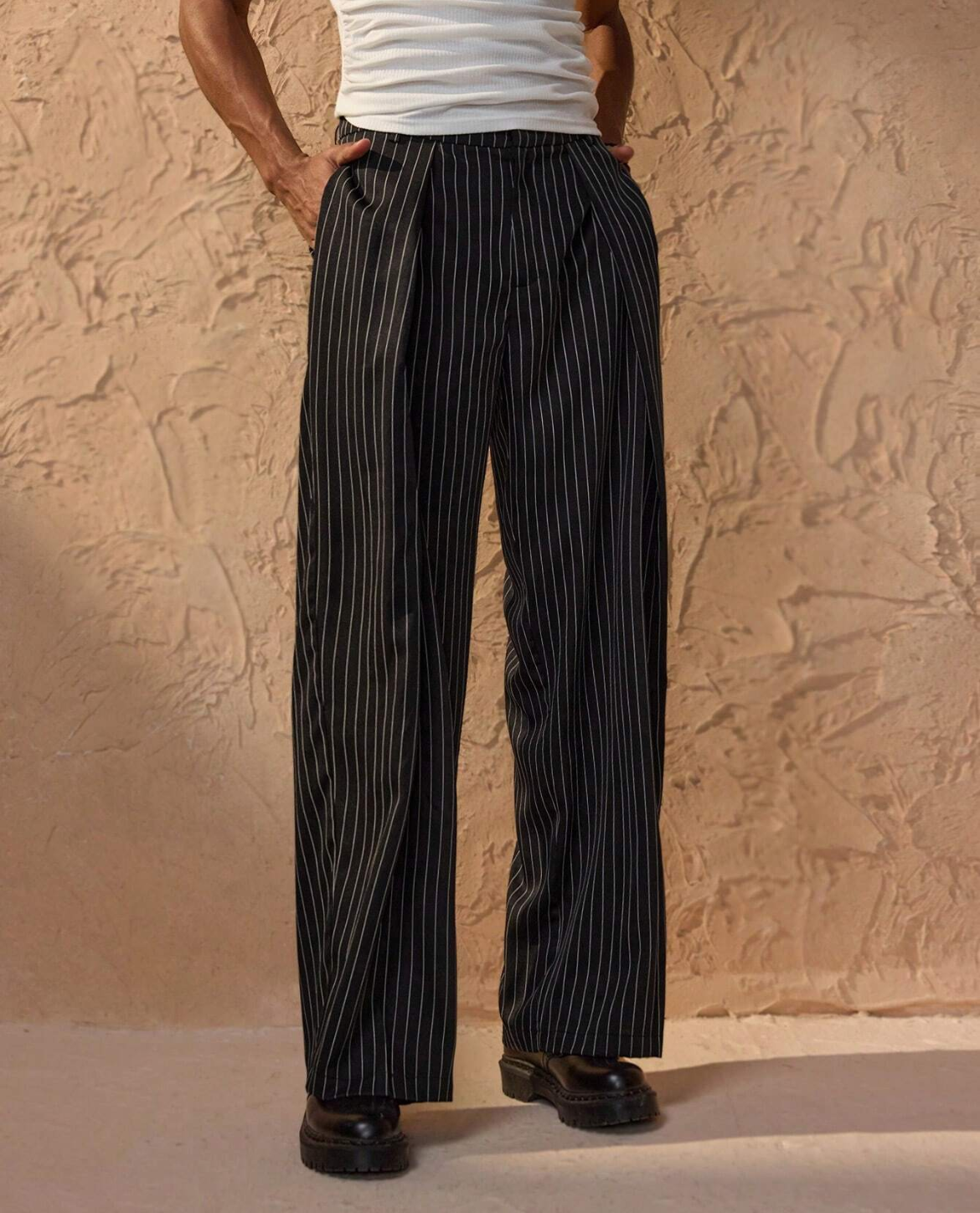 Person wearing black pinstripe pants against a beige textured wall.