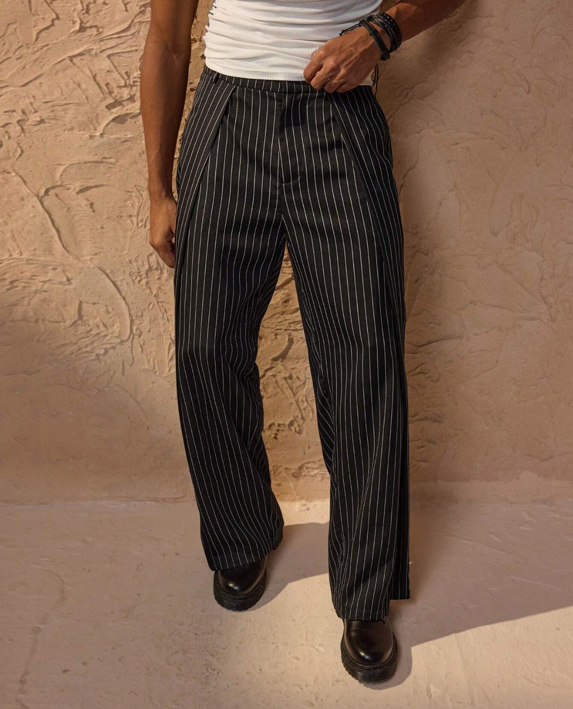 Person wearing black pinstripe pants against a beige wall