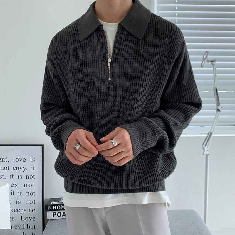 Person wearing a dark gray zip-up sweater over a white shirt, standing indoors.